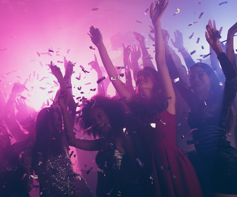 party-goers raise their hands and smile while confetti falls from the ceiling