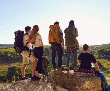 a group of hikers look down on an open field from a hill top